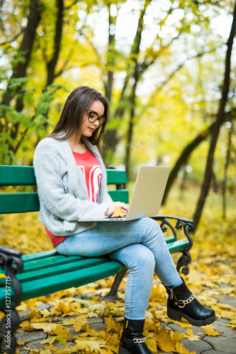 Young happy girl students working on laptop in autumn park
