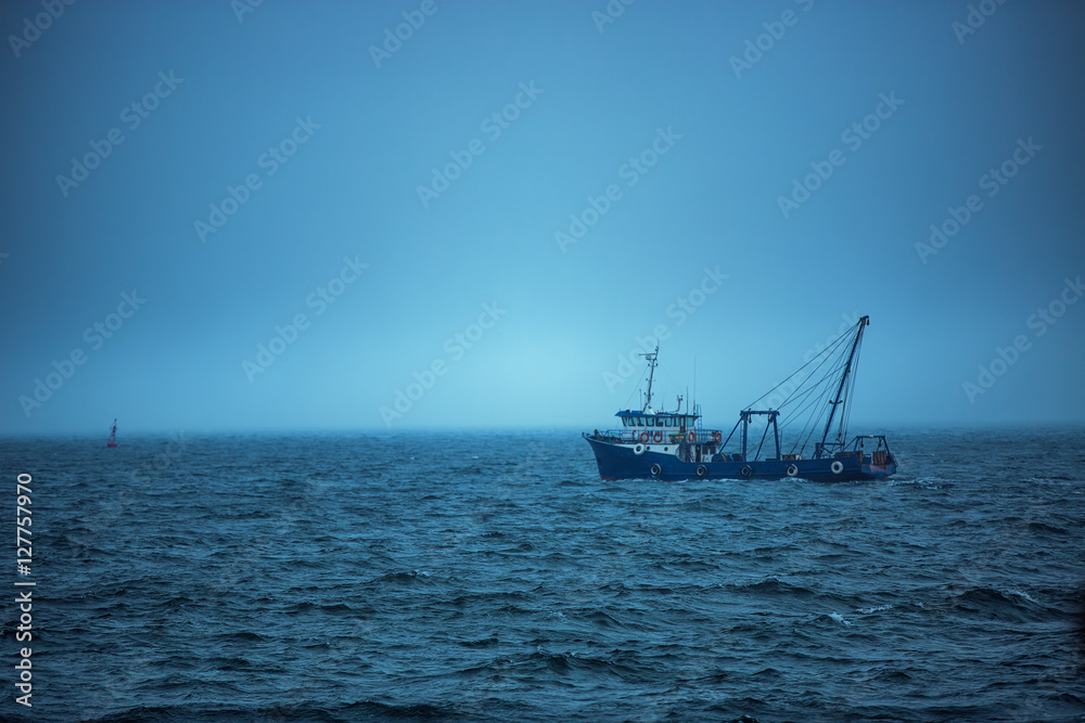 Trawler fishing boat sailing in open waters on a cold and foggy