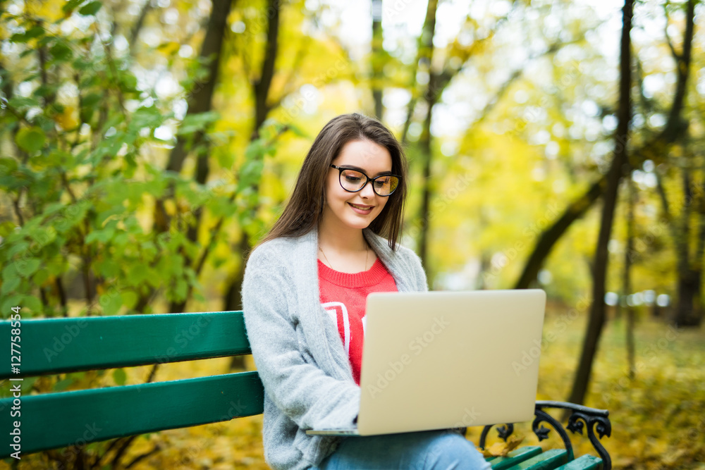 Young happy girl students working on laptop in autumn park Young happy girl students working on laptop in autumn park