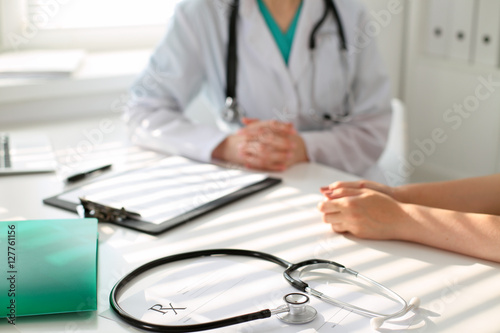 Stethoscope next to hand of doctor reassuring her female patient. Medical ethics and trust concept