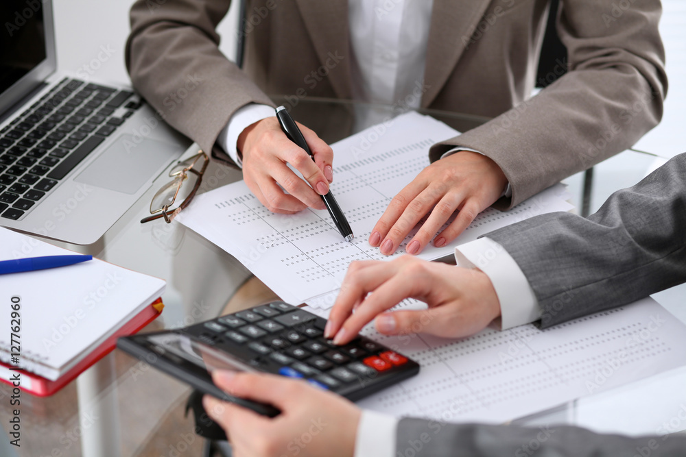 Two female accountants counting on calculator income for tax form completion hands closeup. Internal Revenue Service inspector checking financial document. Planning budget, audit concept Two female accountants counting on calculator income for tax form completion hands closeup. Internal Revenue Service inspector checking financial document. Planning budget, audit concept