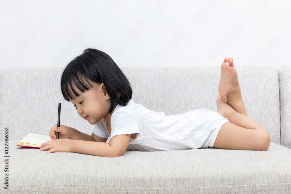 Asian Chinese little girl laying on the sofa writting book Asian Chinese little girl laying on the sofa writting book