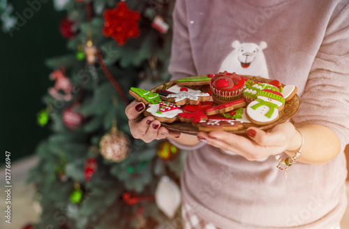 Portrait of beautiful redhead woman holding plate with christmas cakes before dressed up tree