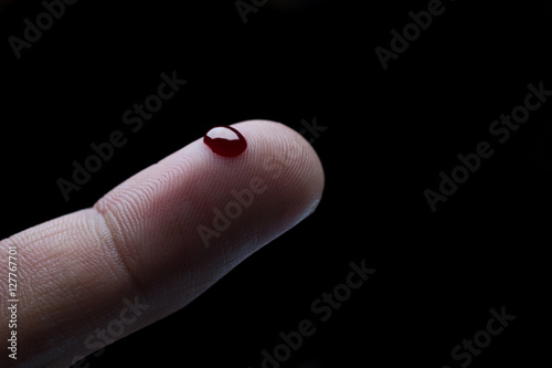 Drop of blood on finger on black background