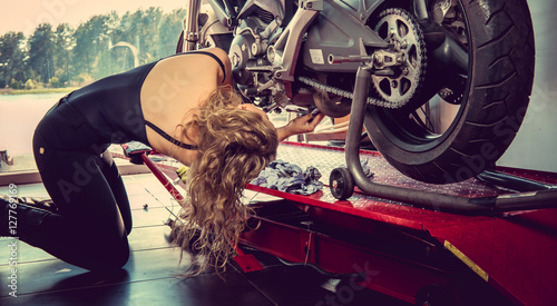 Blonde female repairing motorcycle in a garage.