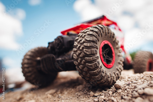 Red crawler wheels outside close-up. Rc car standing on rock, blue sky with clouds on background
