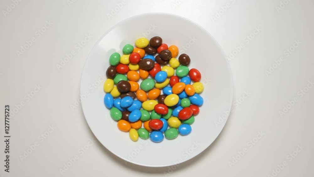 TOP VIEW: Colorful candies appear on a white dish on a white table (stop motion) TOP VIEW: Colorful candies appear on a white dish on a white table (stop motion)