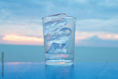 A glass with ice and sunset at sea with quiet feel or blue tone on the background