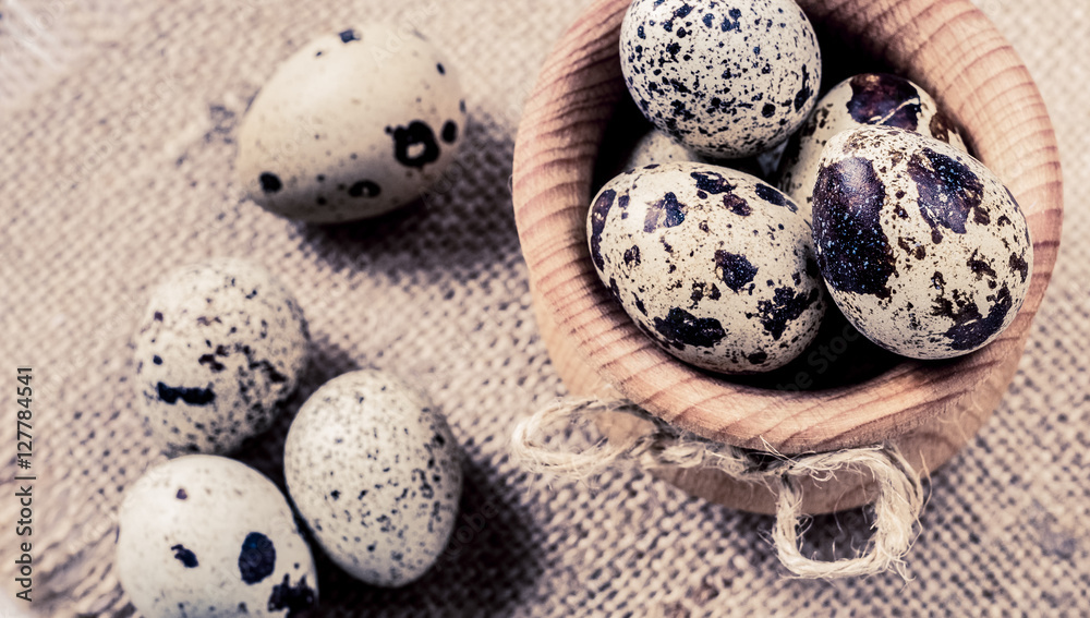 Obraz premium raw quail eggs in a wooden bowl on burlap background