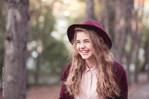 Laughing teen girl 14-16 year old wearing stylish hat and winter jacket outdoors. Looking away. Positive emotions.
