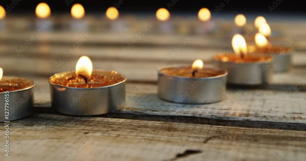 Close-up of burning candles kept in row on wooden plank Close-up of burning candles kept in row on wooden plank