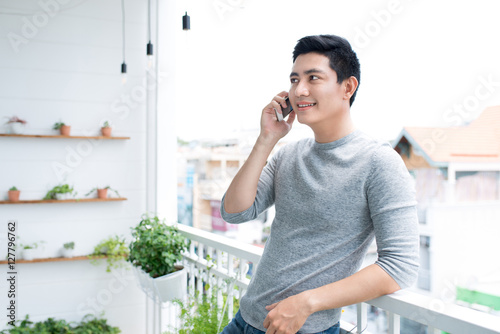 Man talking on smartphone standing on balcony at home.