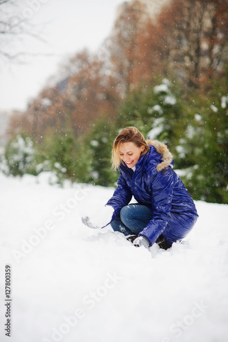 Young woman in the winter park begins to build a snowman. I