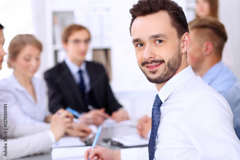 Portrait of cheerful smiling businessman against a group of people at meeting. Portrait of cheerful smiling businessman against a group of people at meeting.