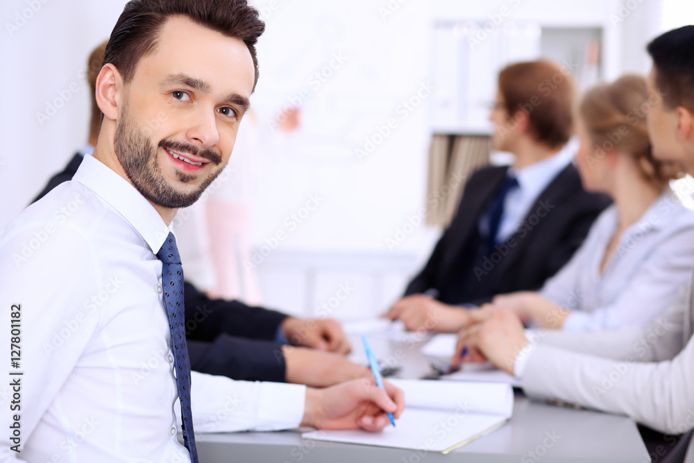 Portrait of cheerful smiling businessman against a group of people at meeting. Portrait of cheerful smiling businessman against a group of people at meeting.