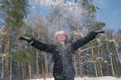 Young beautiful smiling woman throwing snow in the air in winter holidays