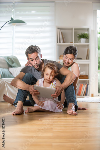 At home, a family sitting on wooden floor while using a tablet