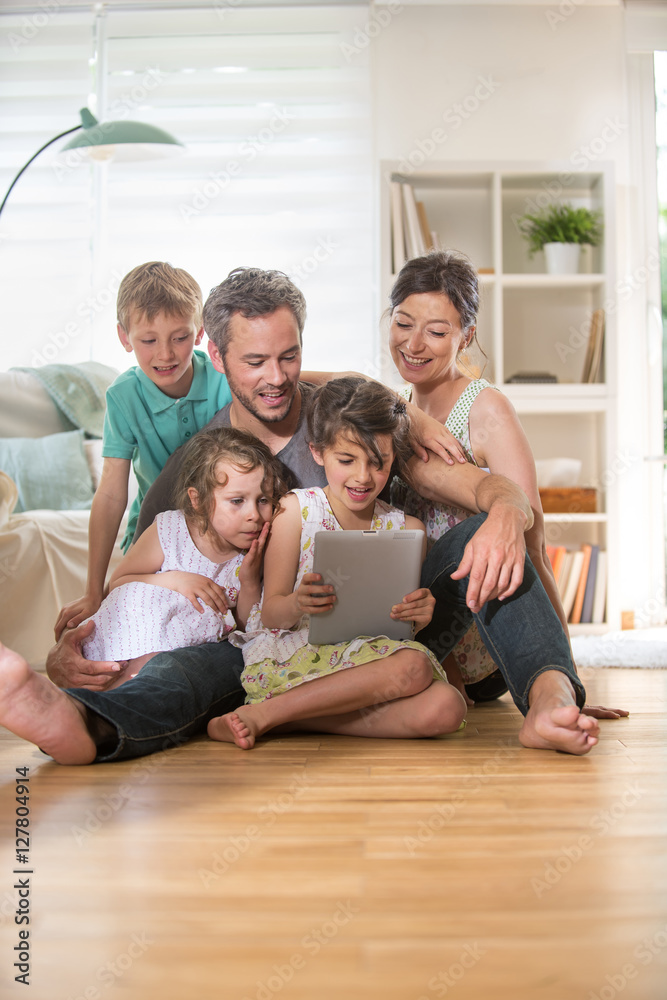 At home, a family sitting on wooden floor while using a tablet