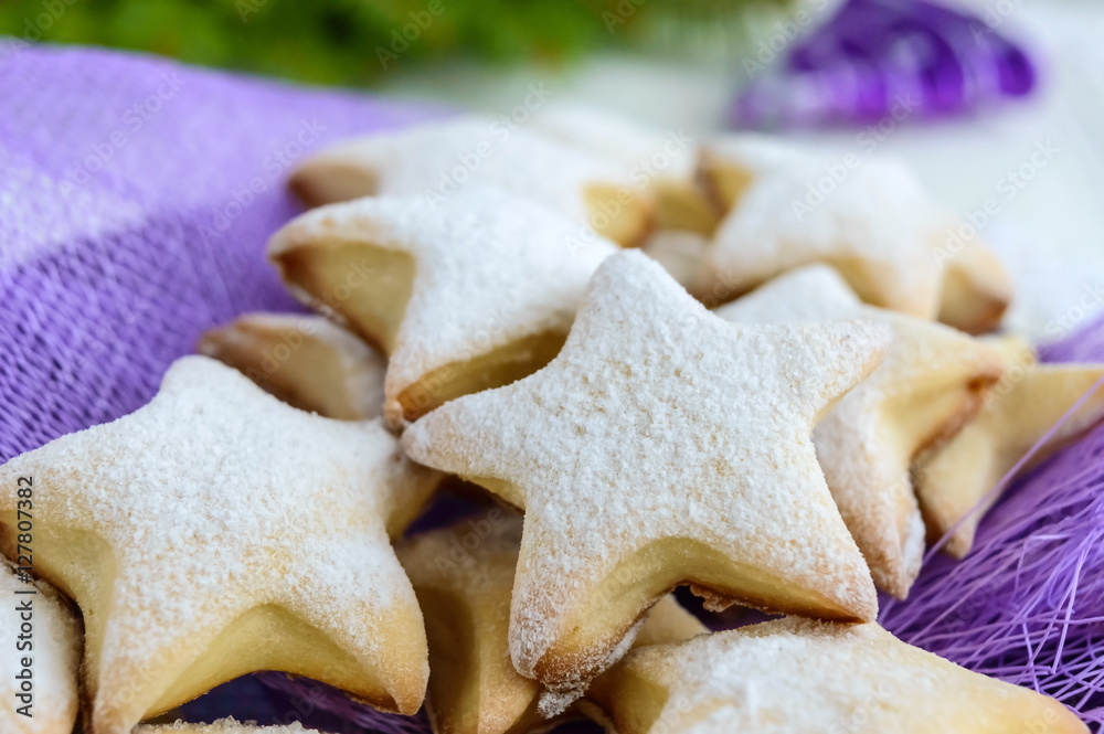 Homemade vanilla cookies in star-shaped decoration with powdered sugar on a purple napkin. Close up