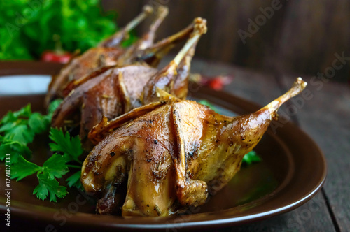 Roasted quail on a spit. Serving on a ceramic plate with greens. Close-up. Holiday menu.