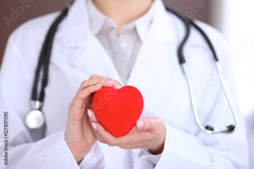Female doctor with stethoscope holding heart. Patients couple sitting in the background