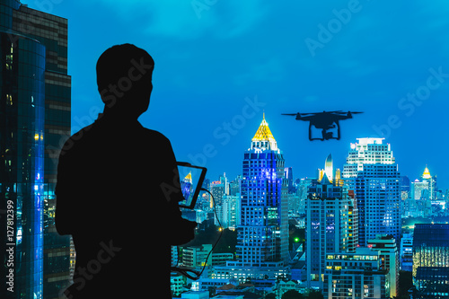 Silhouette of Man using drone to monitor the city at night.