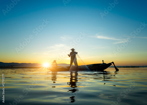 Silhouette of asian fisherman on wooden boat ,fisherman in action throwing a net for catching freshwater fish in nature river, traditional fishermen at the sunset near Galle in Sri Lanka.