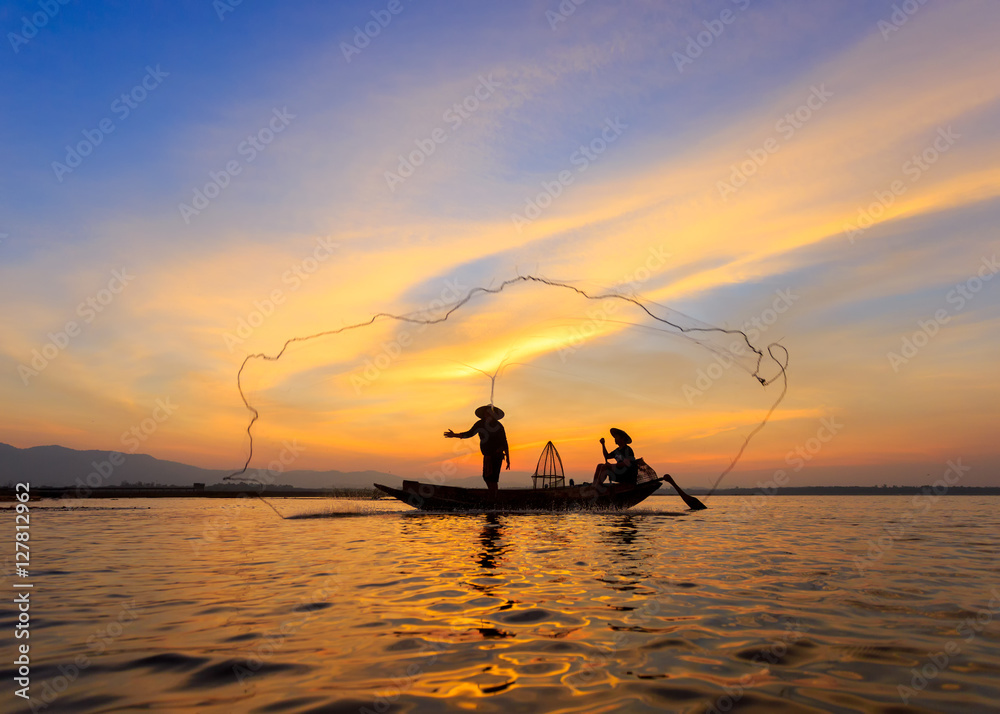 Silhouette of asian fisherman on wooden boat ,fisherman in action throwing a net for catching freshwater fish in nature river, traditional fishermen at the sunset near Galle in Sri Lanka.