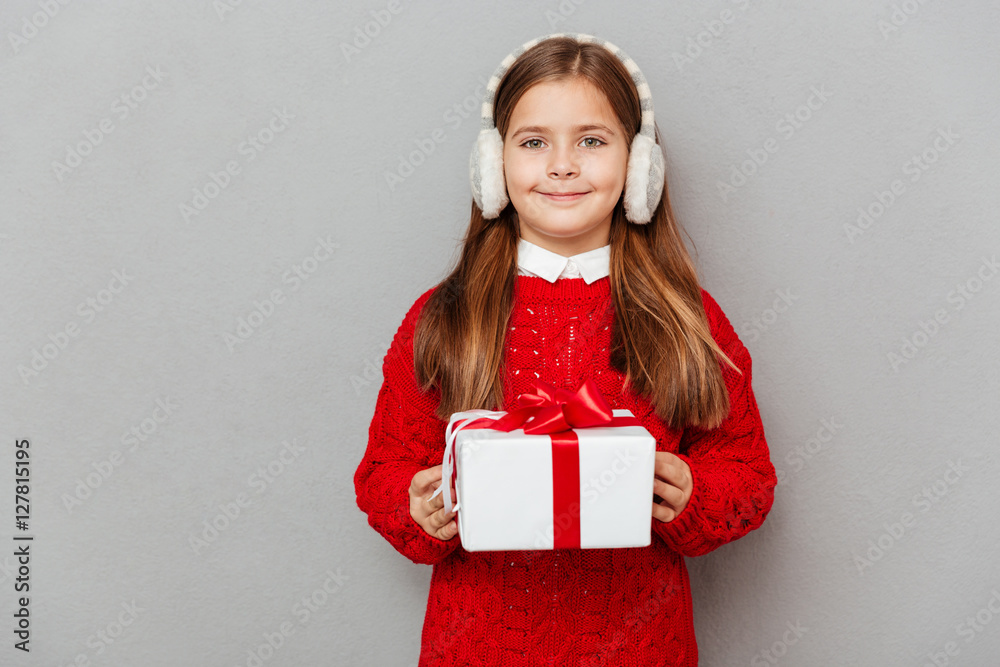 Fototapeta premium Happy little girl in sweater and earmuffs with present box