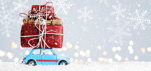 Blue retro toy car delivering Christmas or New Year gifts on festive gray background