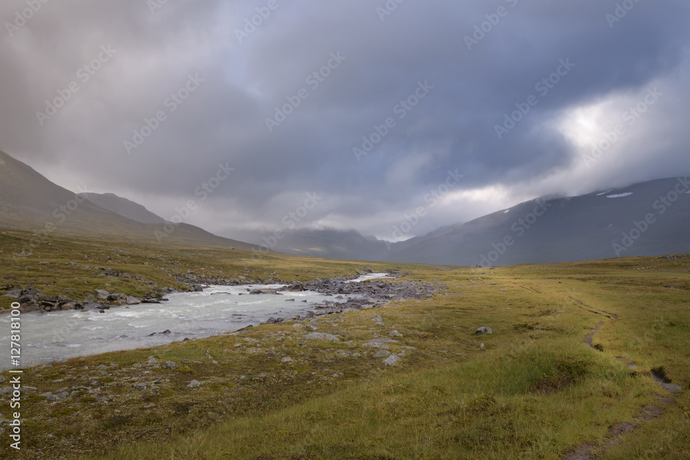 Walking trail beside flowing river in cloudy and moody atmosphere Walking trail beside flowing river in cloudy and moody atmosphere