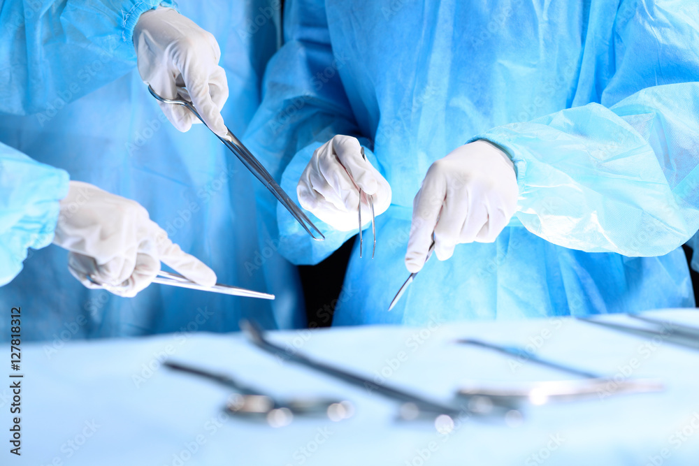 Fototapeta premium Medical team performing operation. Group of surgeon is working in operating theatre toned in blue