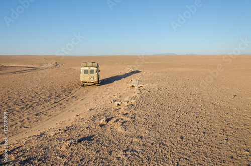 4x4 offroad vehicle driving in empty flat and rocky Namib Desert of Angola.