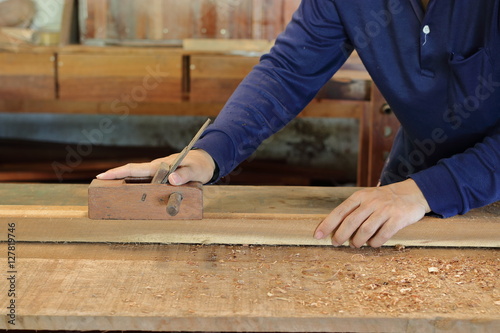 Hand of worker working with a hand planer on a plank of wood.