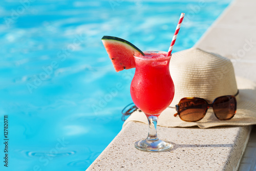 Fresh glass of water-melon smoothie drink with sunglasses, straw hat and slippers on border of a swimming pool - holiday tropical concept