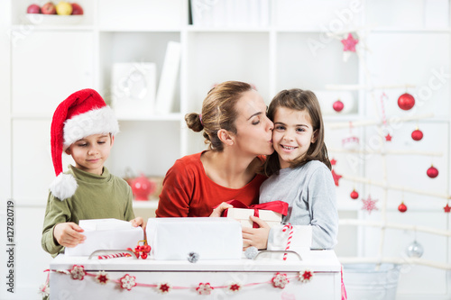 Two kids and their mother are opening Christmas pressents in their lliving room. photo