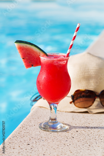 Fresh glass of water-melon smoothie drink with sunglasses, straw hat and slippers on border of a swimming pool - holiday tropical concept
