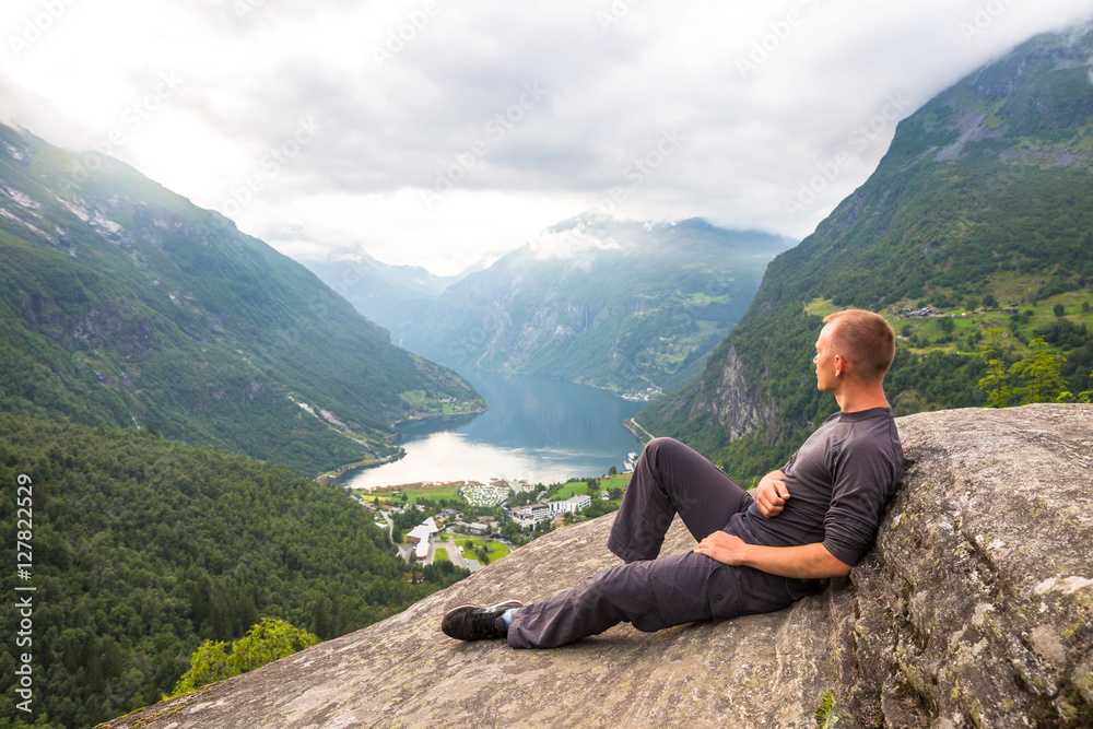 Young men relax on Geiranger fjord. Happy friends enjoy beautiful lake and good weather in Norway.