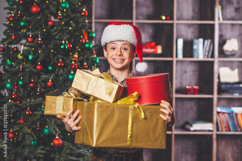 Christmas concept. New Year. Happy child holding a Christmas present. Boy with Christmas gifts, Christmas tree in the background. Boy and a lot of Christmas gifts