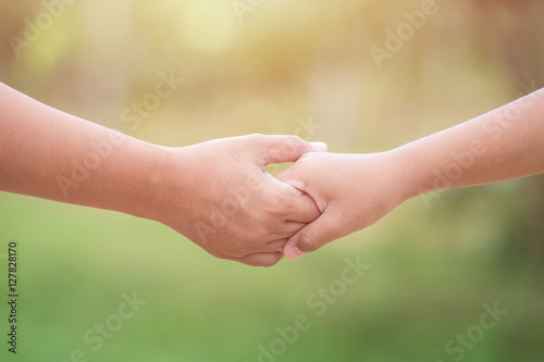 Two hands holding together. Help or support concept. On green bl © SKT Studio