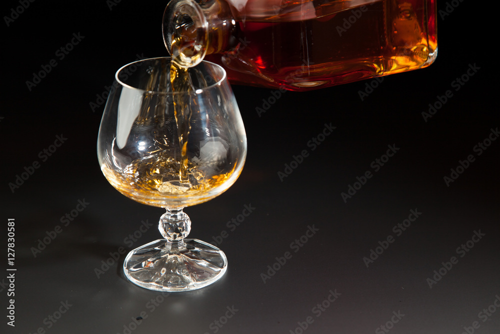 Cognac is poured from a bottle into  glass