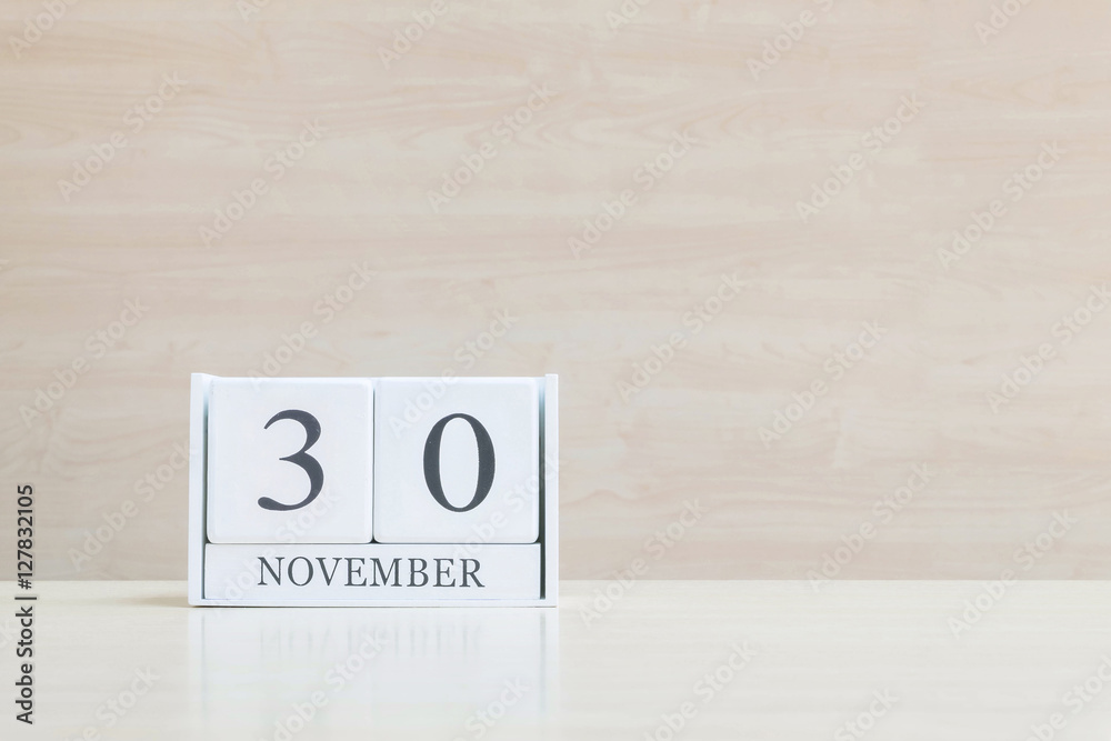 Closeup surface white wooden calendar with black 30 november word on blurred brown wood desk and wood wall textured background with copy space , selective focus at the calendar Closeup surface white wooden calendar with black 30 november word on blurred brown wood desk and wood wall textured background with copy space , selective focus at the calendar