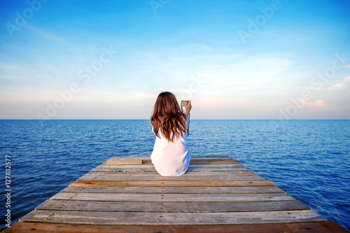 Girl sitting alone and hand holding camera on a the wooden bridg