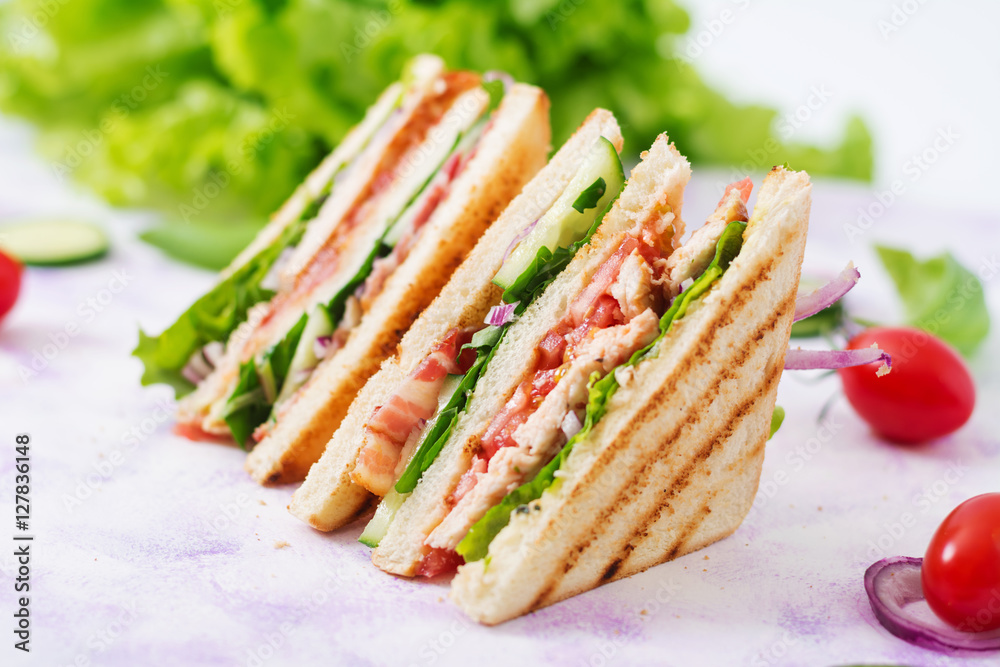 Club sandwich with chicken breast, bacon, tomato, cucumber and herbs