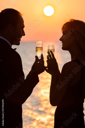 couple souriant qui trinque avec du champagne au coucher du soleil