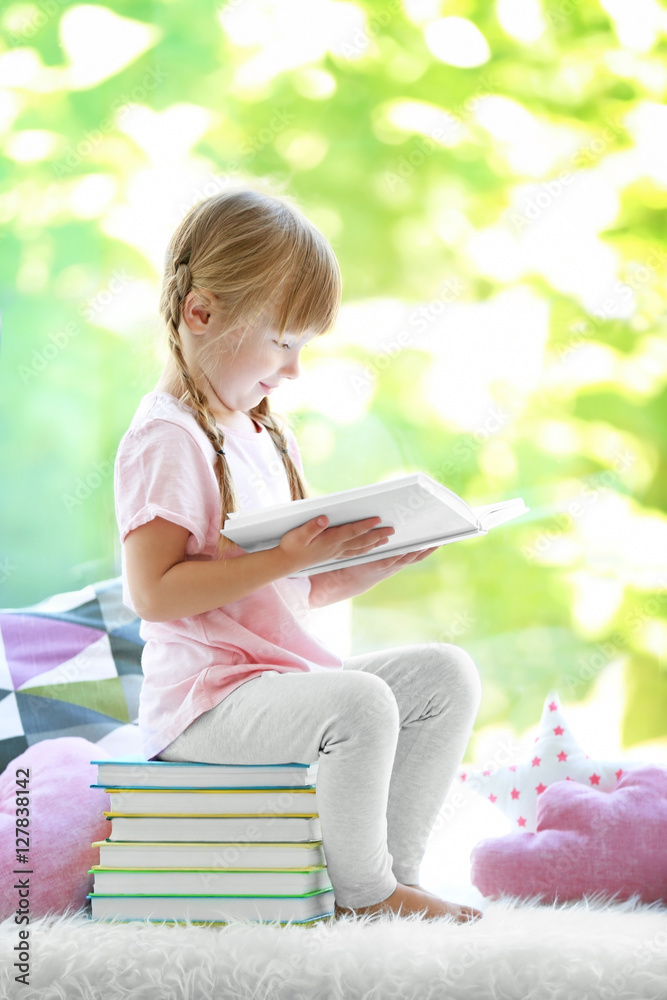 Φωτογραφία Beautiful little girl sitting on pile of books near window