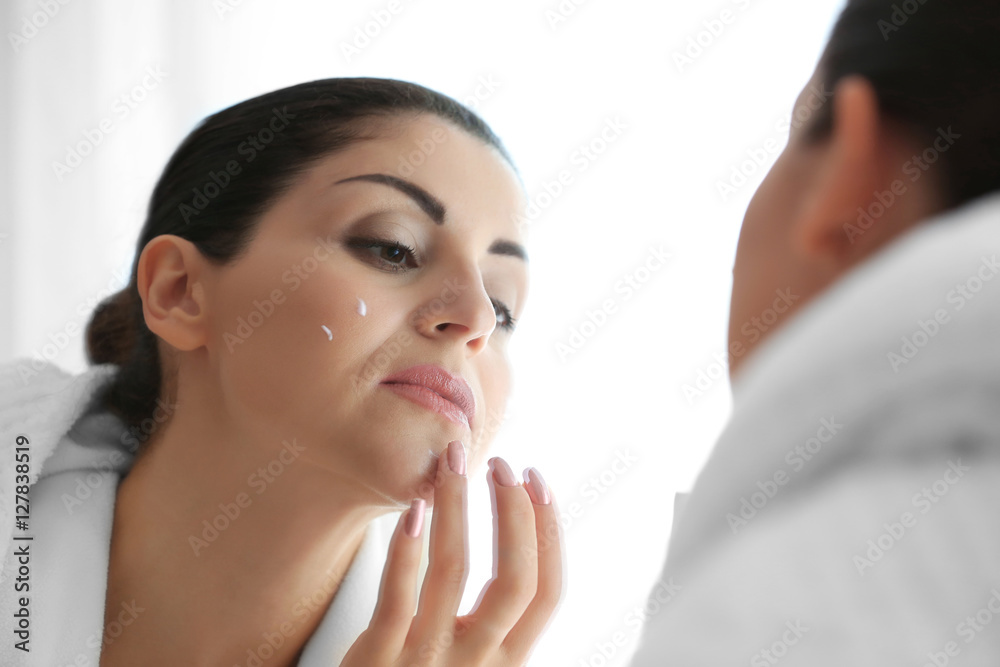Adult woman applying cream on face in mirror reflection Adult woman applying cream on face in mirror reflection