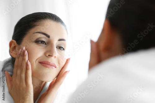 Adult woman checking her face in mirror on light background