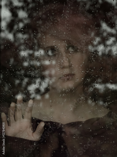 Frau steht am  Fenster bei Regen