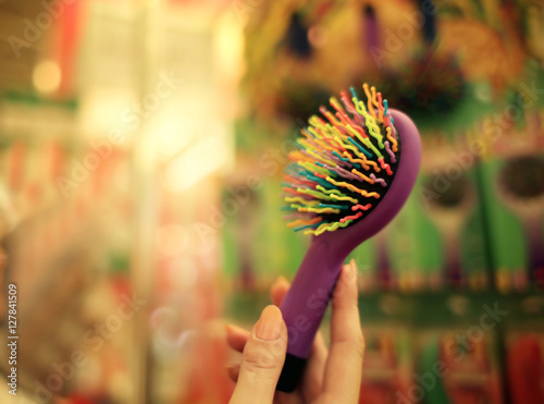 Female hand holding colourful barber comb in cosmetic store